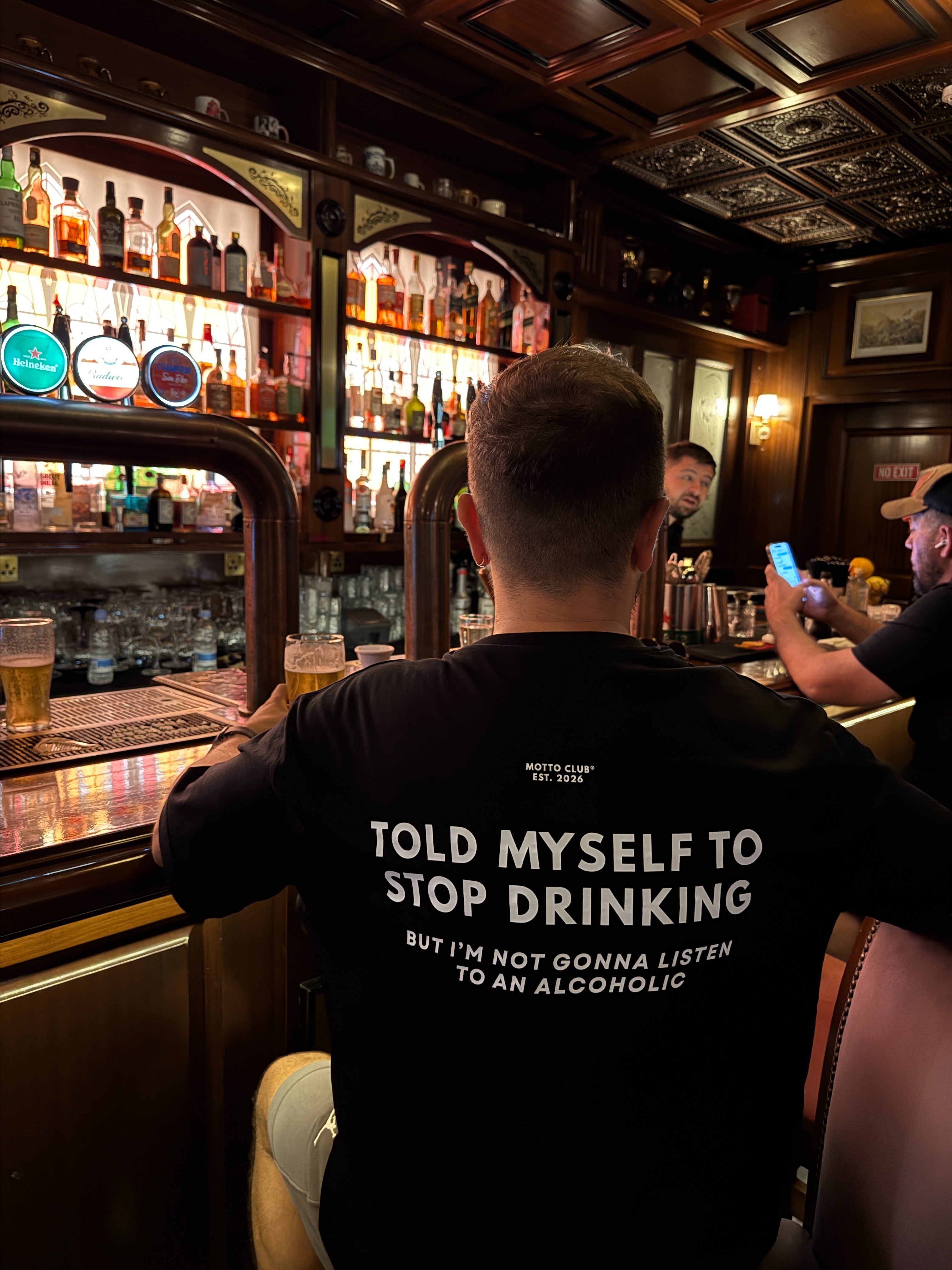 White Motto Club tee in a Valletta crowd. The back print reads life sucks but I suck better.