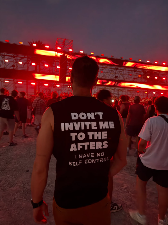 Black Motto Club tank in a Malta festival crowd, red stage light behind.